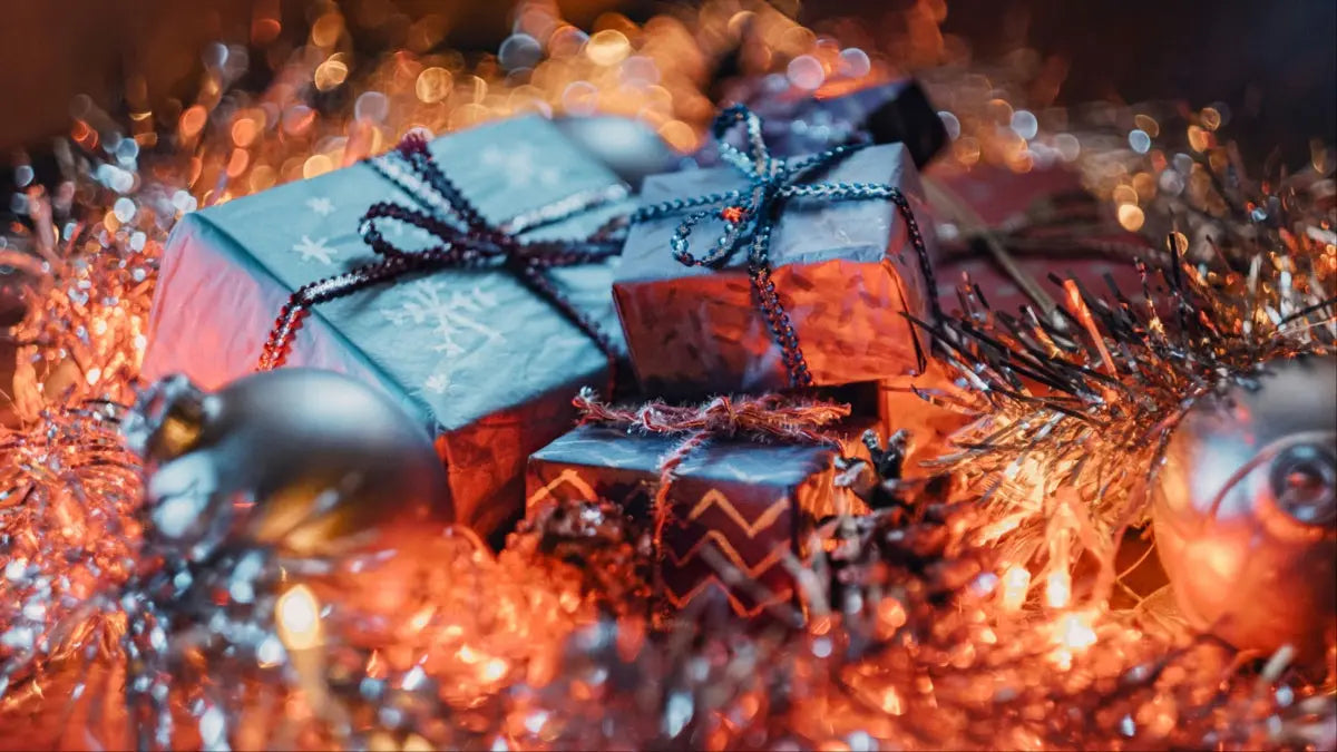 A pile of wrapped Christmas gifts surrounded by fairy lights and tinsel