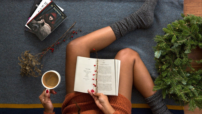 Woman lounges and reads a book in cosy socks, cup of tea, surrounded by Christmas decorations