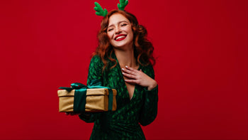 Gifts for Her: woman against red background dressed in green holding Christmas present