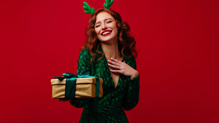 Gifts for Her: woman against red background dressed in green holding Christmas present