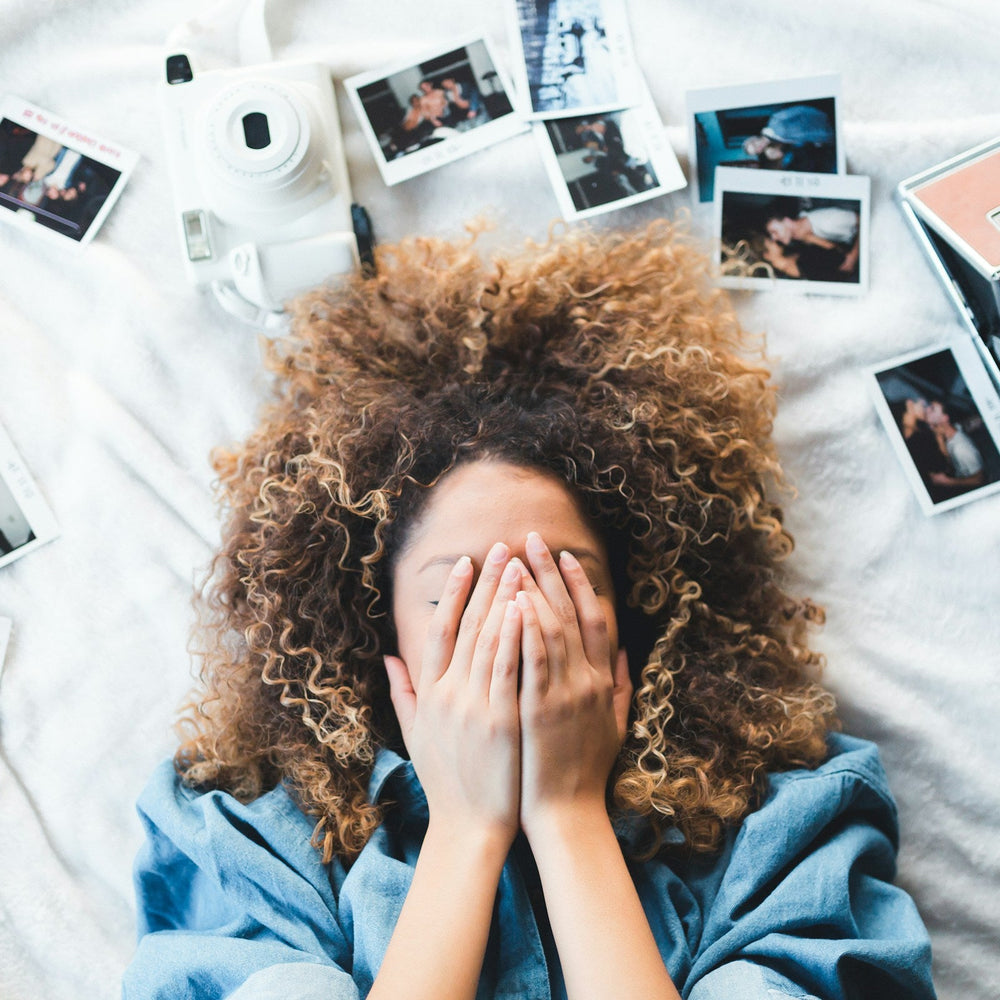 woman lying in bed with eyes covered, surrounded by personal photos 