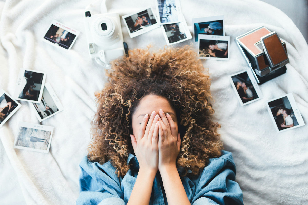 woman lying in bed with eyes covered, surrounded by personal photos 