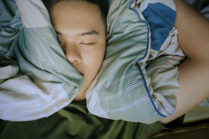 man sleeping in bed with ears covered by bedding
