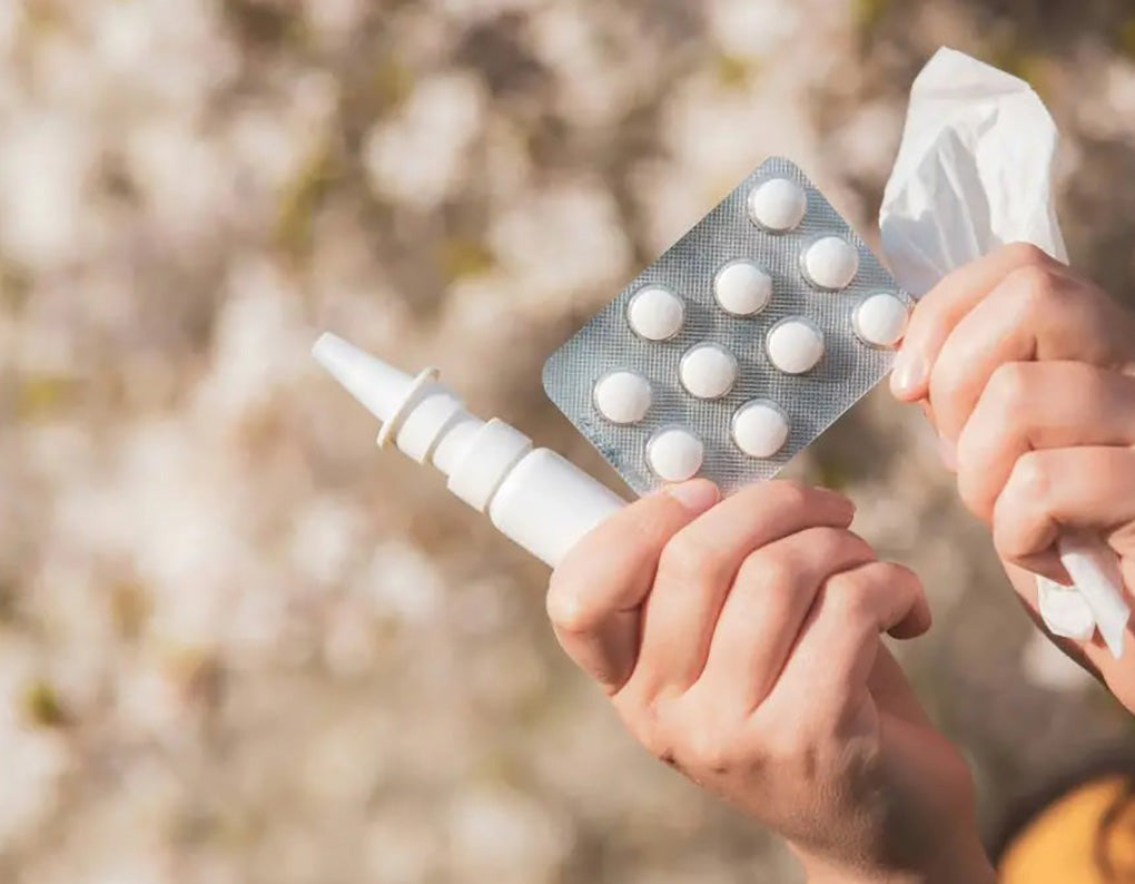 hands holding up a blister pack of tablets, nasal spray,  and tissues
