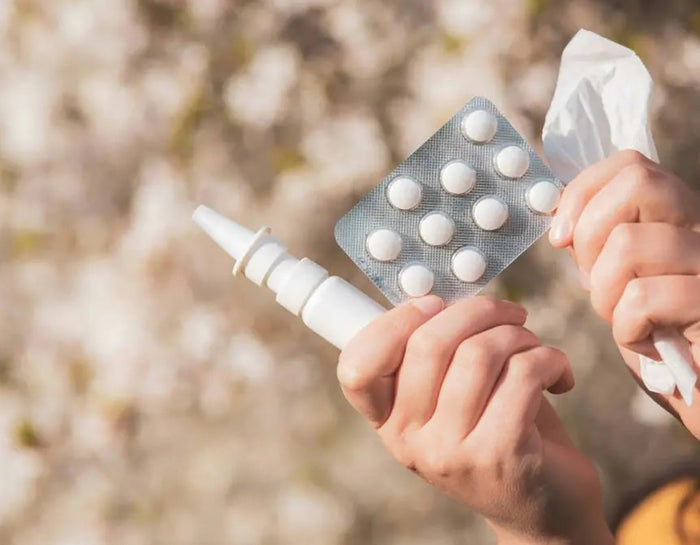 hands holding up a blister pack of tablets, nasal spray,  and tissues