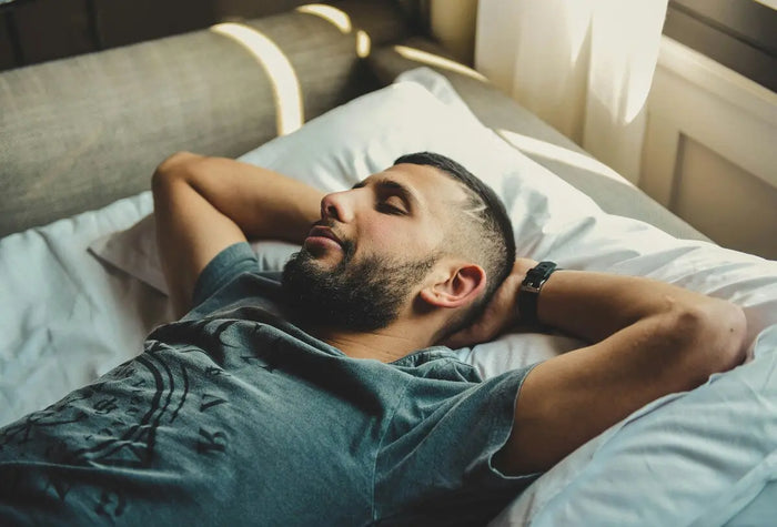 man relaxing in bed with arms crossed behind head